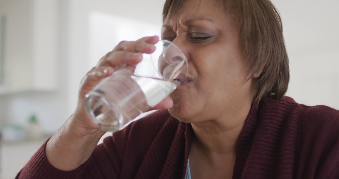 Mature Woman Drinking Water with Displeased Expression at Home - Free Images, Stock Photos and Pictures on Pikwizard.com