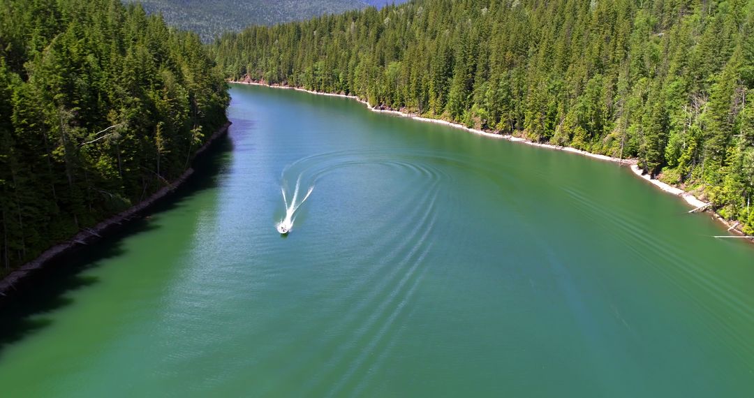 An aerial shot shows a boat cruising, causing ripples on a serene, forest-bordered lake. - Free Images, Stock Photos and Pictures on Pikwizard.com