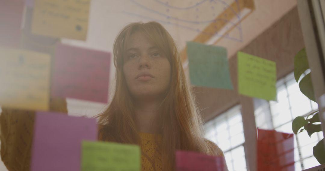 Focused Young Woman Analyzing Colorful Notes on Glass Board in Office - Free Images, Stock Photos and Pictures on Pikwizard.com