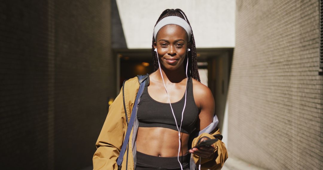 Portrait of african american woman exercising outdoors wearing earphones and smiling to camera - Free Images, Stock Photos and Pictures on Pikwizard.com