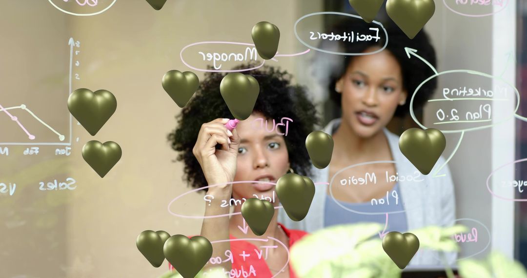 Female Colleagues Collaborating on Glass Board Drawing Flowchart with Gold Heart Overlays