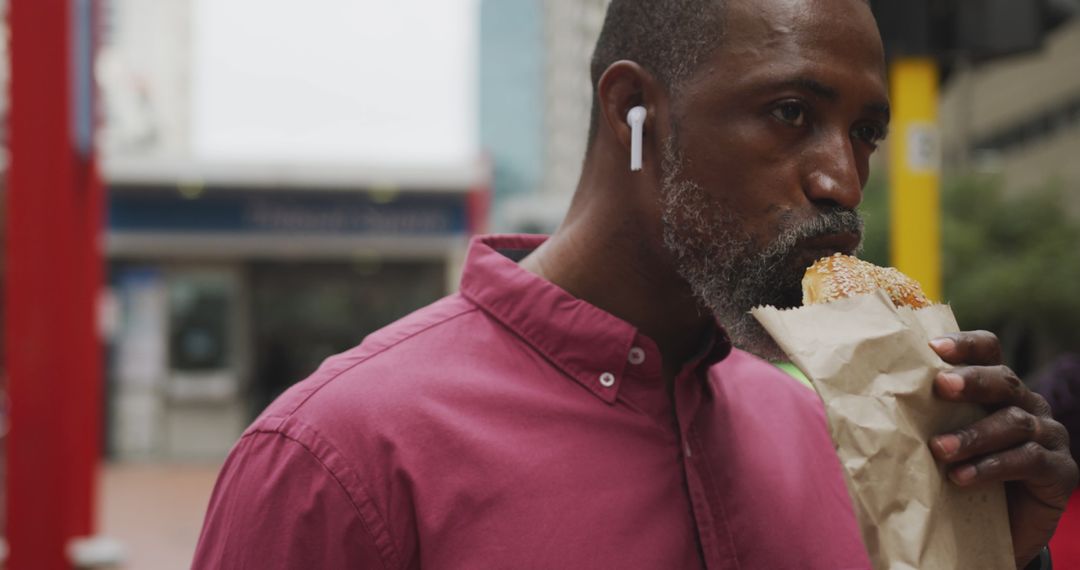 Man Wearing Earbuds Eating Sandwich on City Street - Free Images, Stock Photos and Pictures on Pikwizard.com