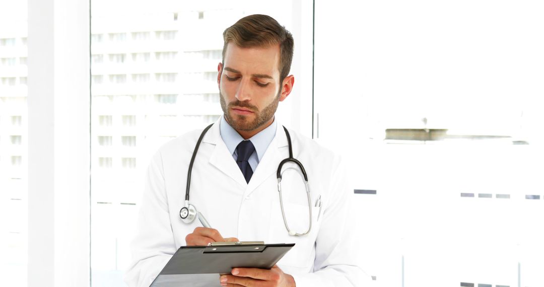 Male Doctor in White Coat Writing on Clipboard in Modern Medical Office - Free Images, Stock Photos and Pictures on Pikwizard.com