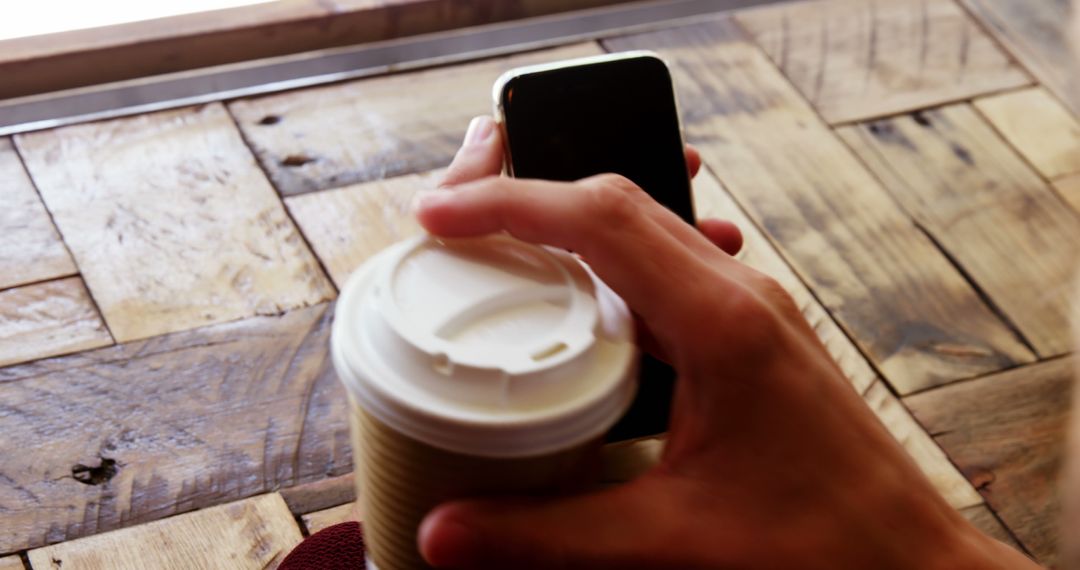 Person Holding Coffee Cup and Smartphone in Cozy Cafe - Free Images, Stock Photos and Pictures on Pikwizard.com