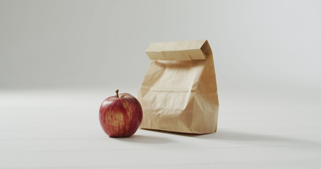 Minimalist Lunch With Brown Bag and Fresh Apple on White Surface