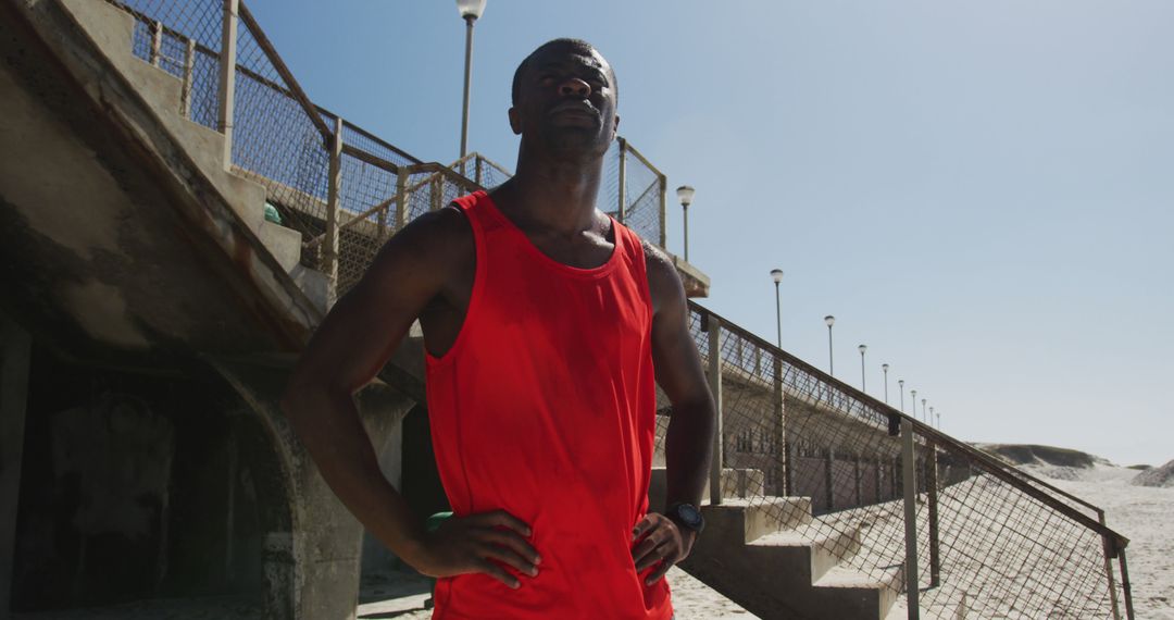 Confident African American man in red tank top posing near beach stairs - Free Images, Stock Photos and Pictures on Pikwizard.com