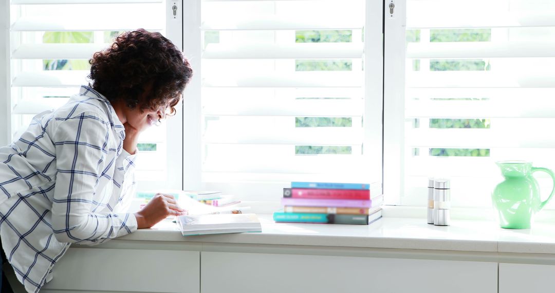 Woman Leaning on Counter Reading Book Near Bright Window - Free Images, Stock Photos and Pictures on Pikwizard.com