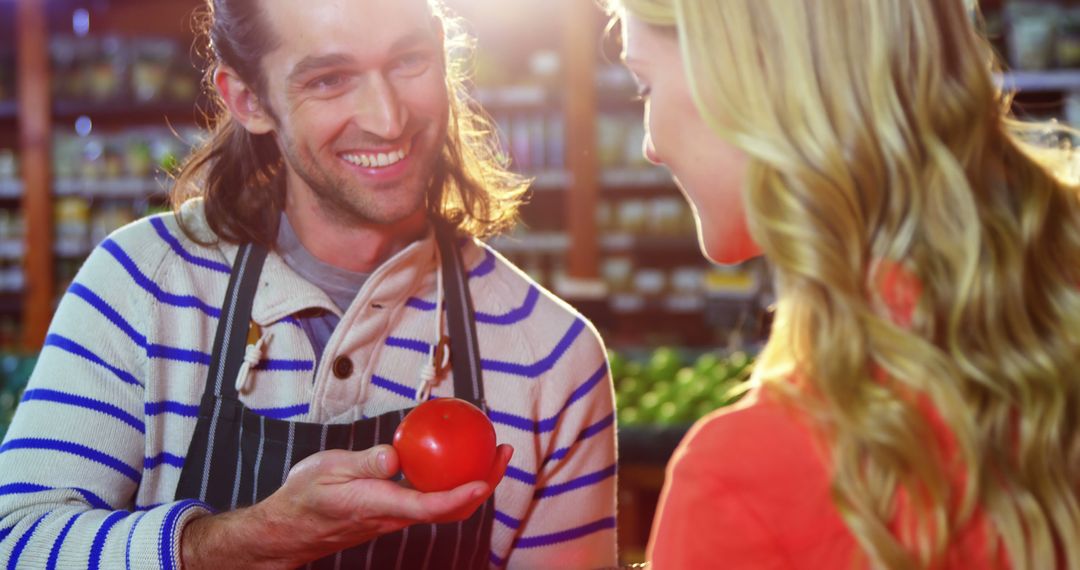 Smiling Grocer Showing Customer Fresh Tomato in Store - Free Images, Stock Photos and Pictures on Pikwizard.com