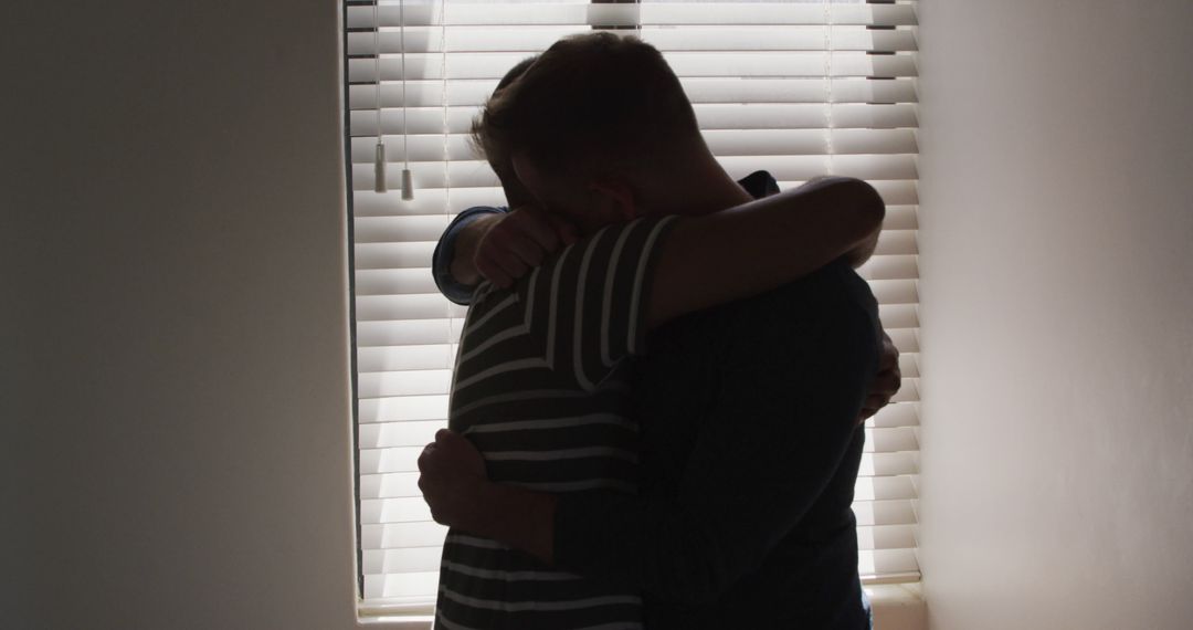 Comforting Hug Between Two People Near Window With Blinds - Free Images, Stock Photos and Pictures on Pikwizard.com