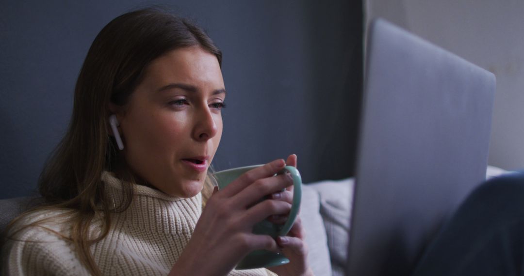 Young Woman in Sweater Drinks Coffee While Working on Laptop - Free Images, Stock Photos and Pictures on Pikwizard.com