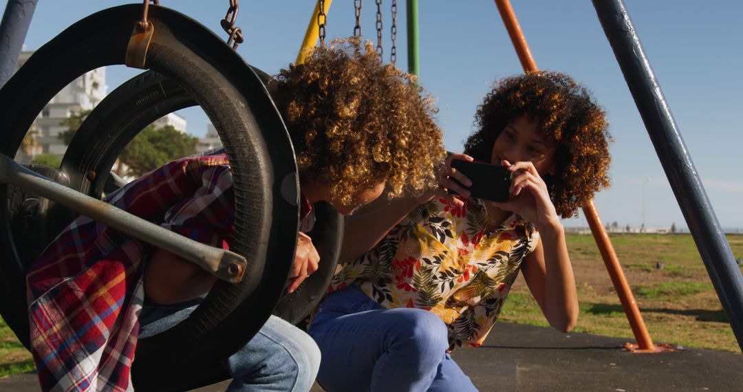 African American Mother Photographing Son Playing on Swing Set in Sunny Park - Free Images, Stock Photos and Pictures on Pikwizard.com