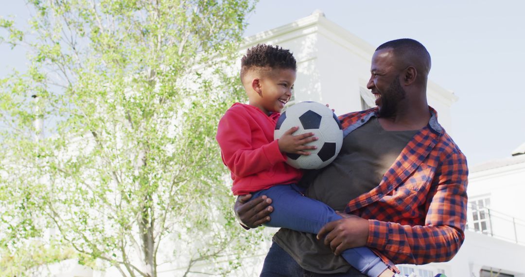 Portrait of happy african american father and his son holding football and embracing in garden - Free Images, Stock Photos and Pictures on Pikwizard.com
