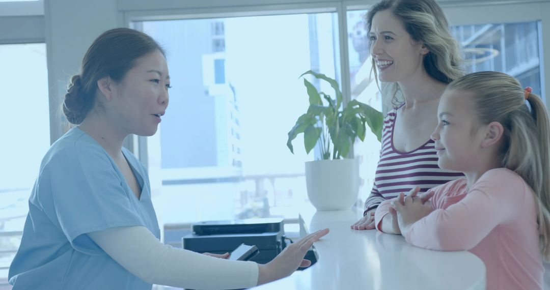 Nurse gesturing while holding documents at reception desk with mother and daughter smiling