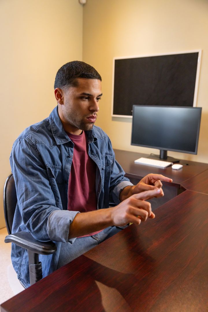 Focused Professional Gesturing at Office Desk with Computer Display