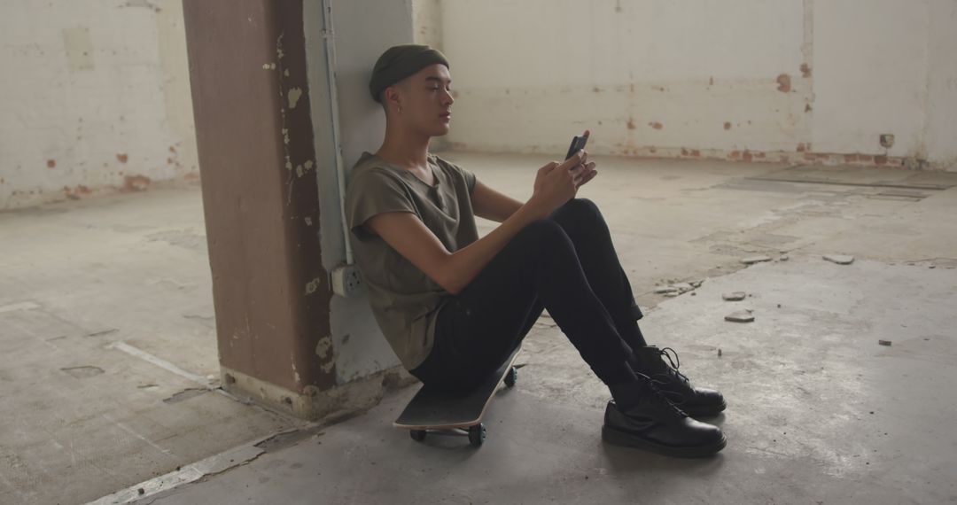 Young Man Sitting Against Pillar Using Smartphone in Abandoned Building - Free Images, Stock Photos and Pictures on Pikwizard.com