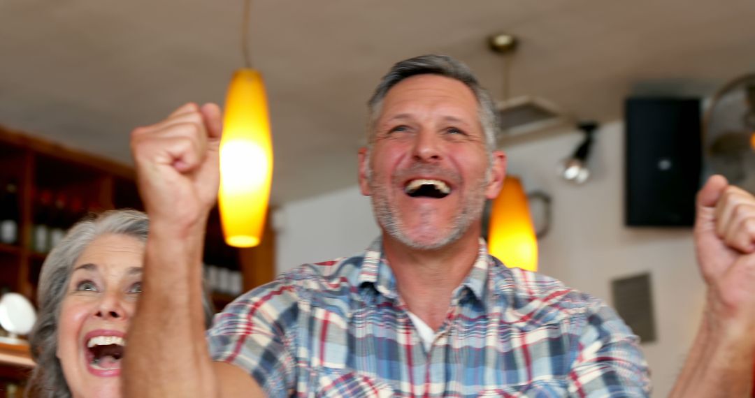 Cheerful middle-aged couple celebrating victory indoors