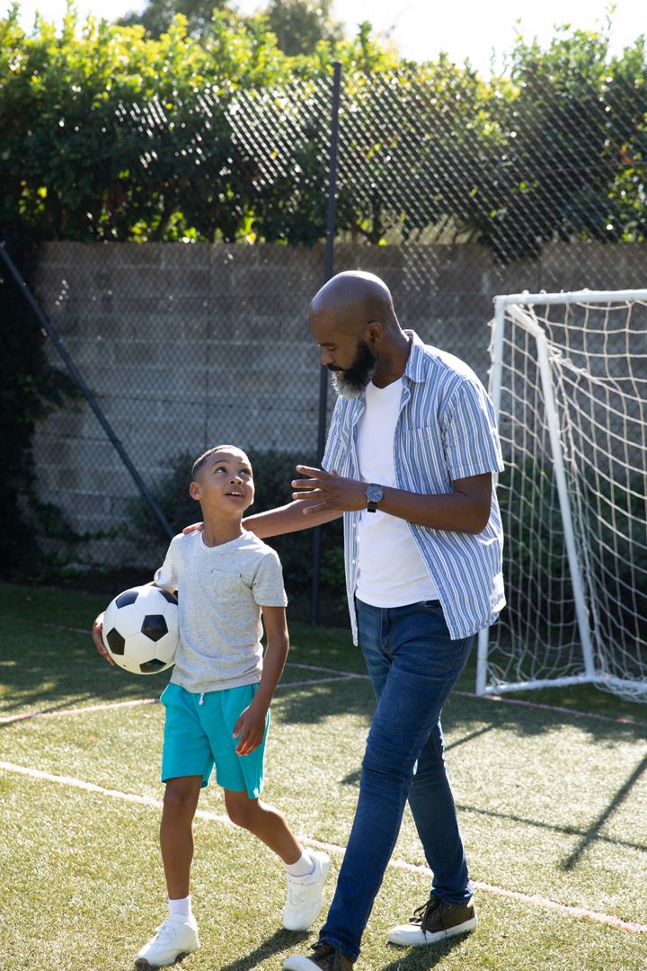 Father and Son Bonding on Soccer Field with Ball under Bright Sunlight