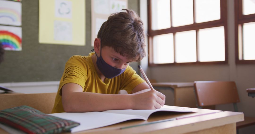 Young Student Wearing Mask in Classroom Writing in Notebook - Free Images, Stock Photos and Pictures on Pikwizard.com