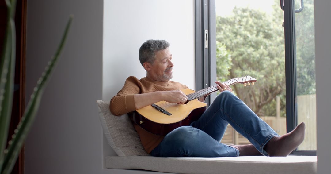 Relaxed Middle-aged Man Playing Acoustic Guitar by Window - Free Images, Stock Photos and Pictures on Pikwizard.com