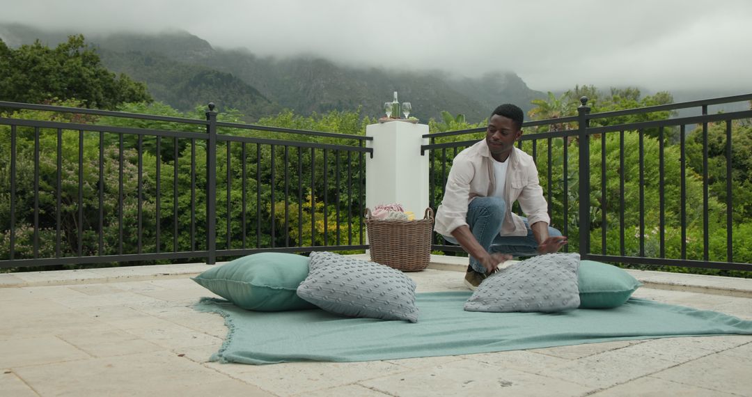 Man Arranging Cushions on Scenic Mountain Terrace for Relaxation