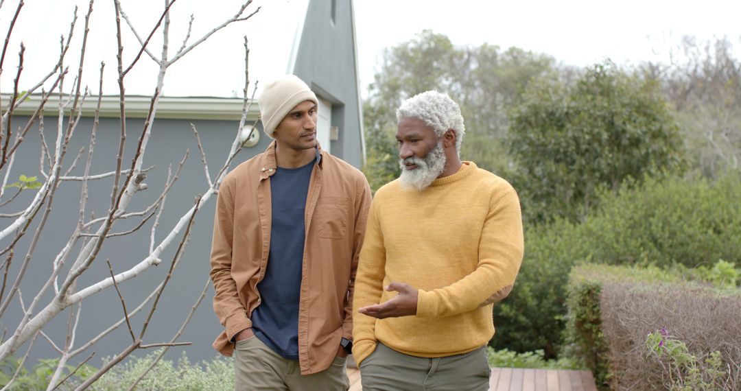 Two men walking and talking on wooden pathway beside modern home with garden and foliage