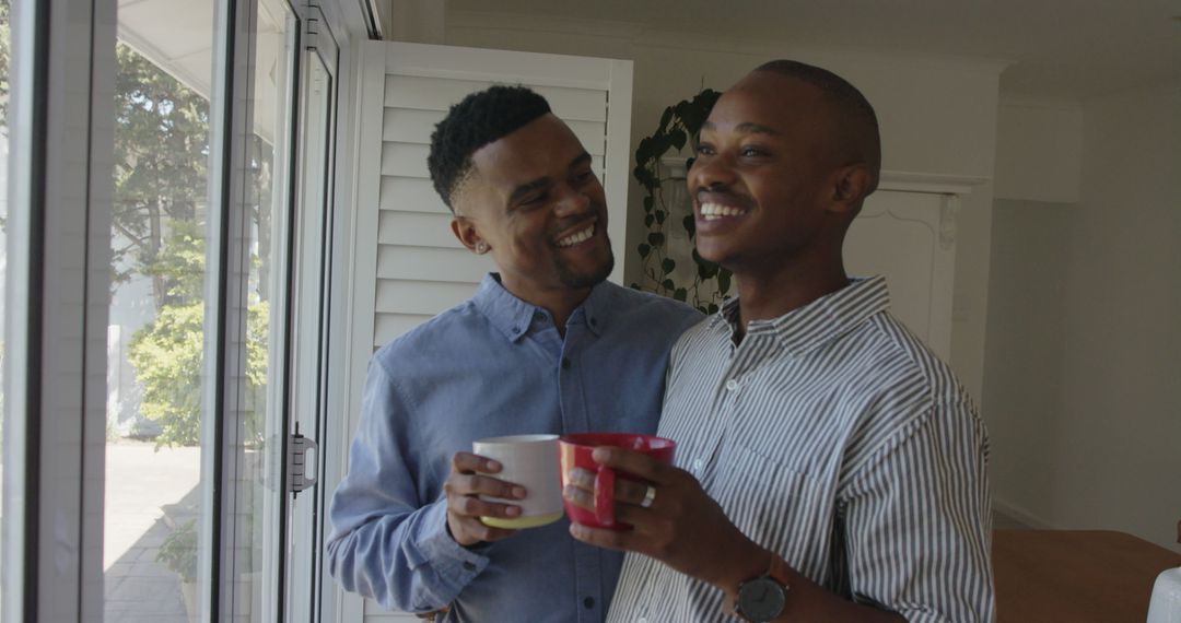 Happy african american gay male couple drinking coffee and laughing at home - Free Images, Stock Photos and Pictures on Pikwizard.com