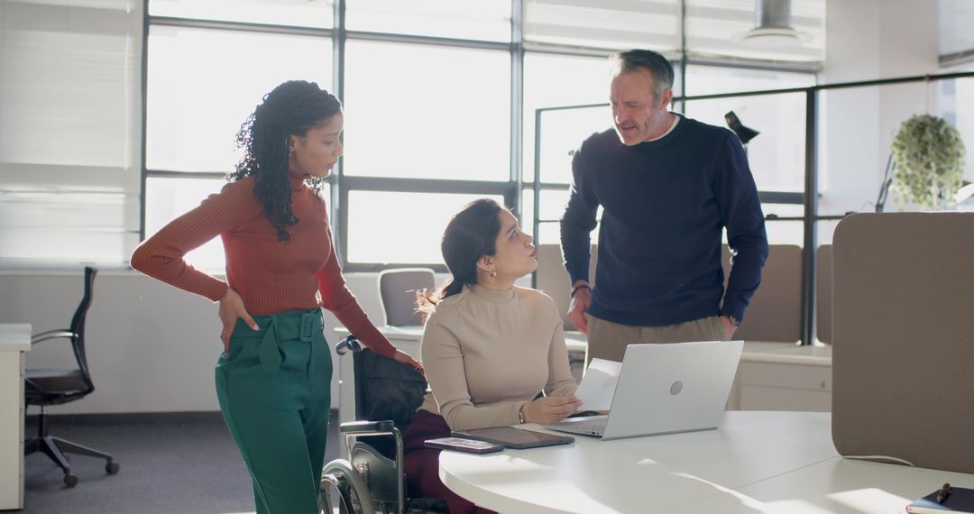 Multicultural team collaborating with employee in wheelchair at modern accessible office