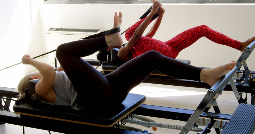 Two Women Doing Pilates Exercises on Reformer Machines at Modern Fitness Studio - Free Images, Stock Photos and Pictures on Pikwizard.com