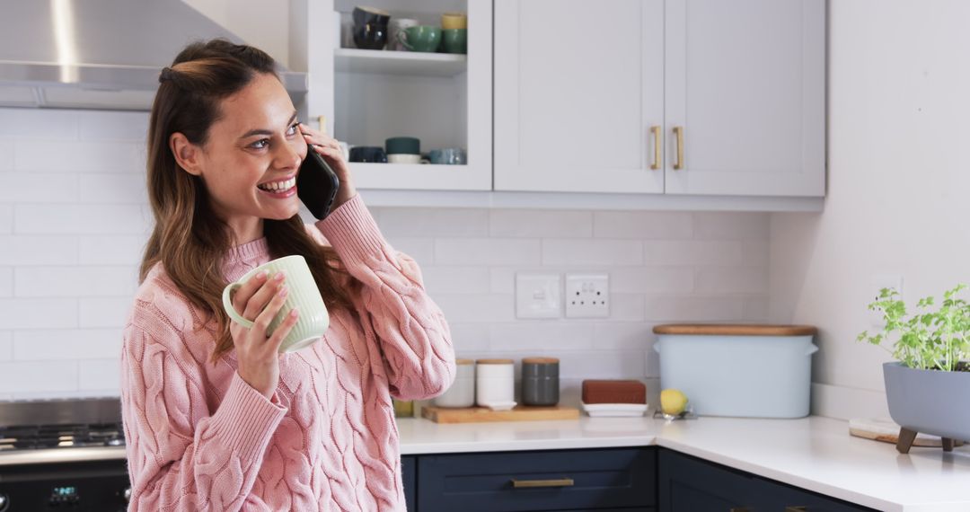 Smiling Woman Holding Mug and Talking on Smartphone in Modern Kitchen