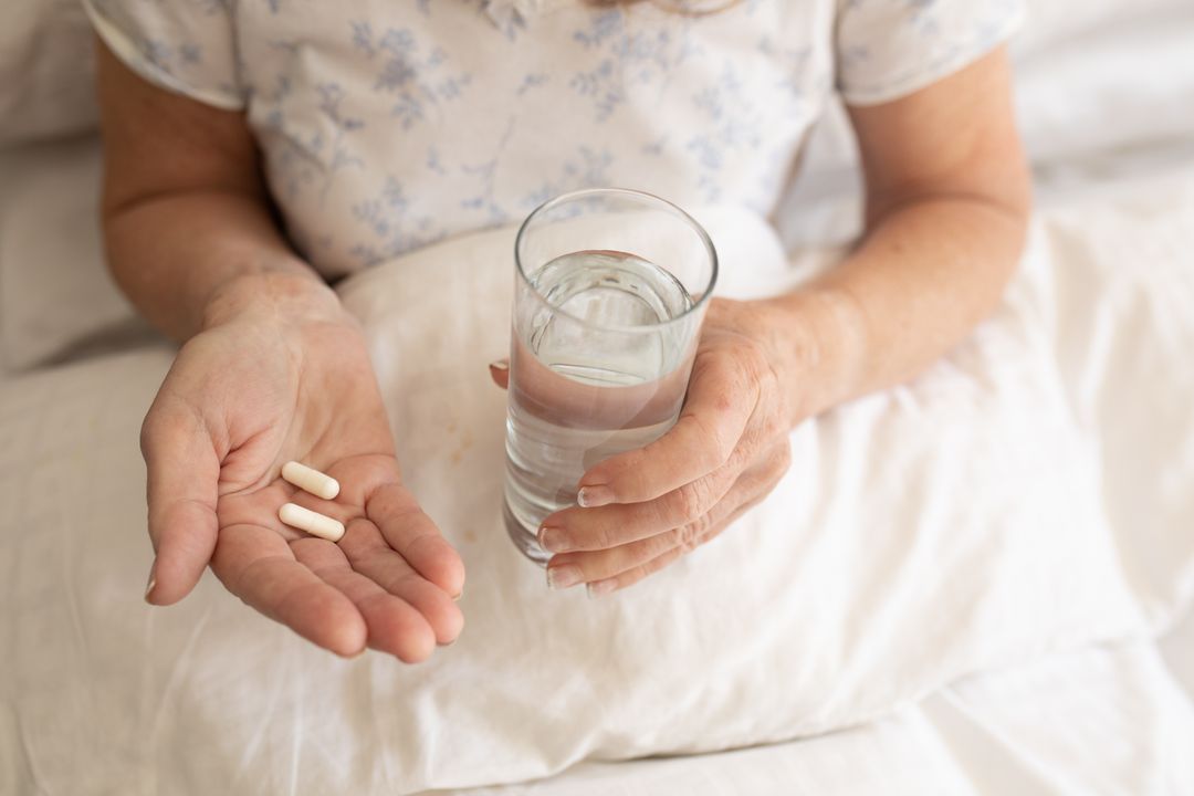 Senior Woman Holding Pills and Water in Bed - Free Images, Stock Photos and Pictures on Pikwizard.com