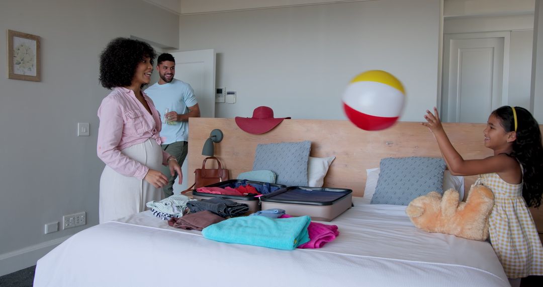 Diverse Family Packing Suitcase While Daughter Plays with Beach Ball