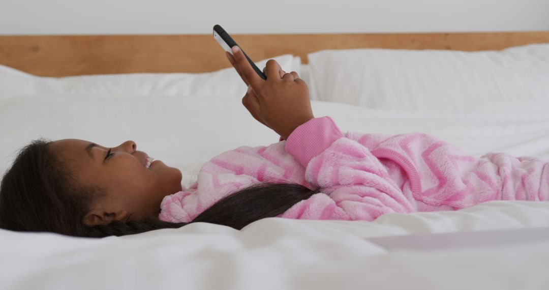 Young Girl Relaxing in Pink Robe While Checking Smartphone in Bed - Free Images, Stock Photos and Pictures on Pikwizard.com