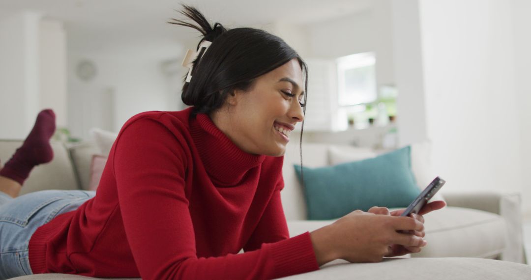 Image of happy biracial woman in hijab lying on sofa and using smartphone - Free Images, Stock Photos and Pictures on Pikwizard.com