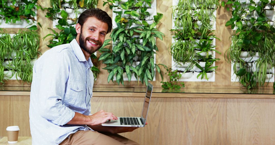 Smiling Man Using Laptop in Modern Indoor Garden Space - Free Images, Stock Photos and Pictures on Pikwizard.com