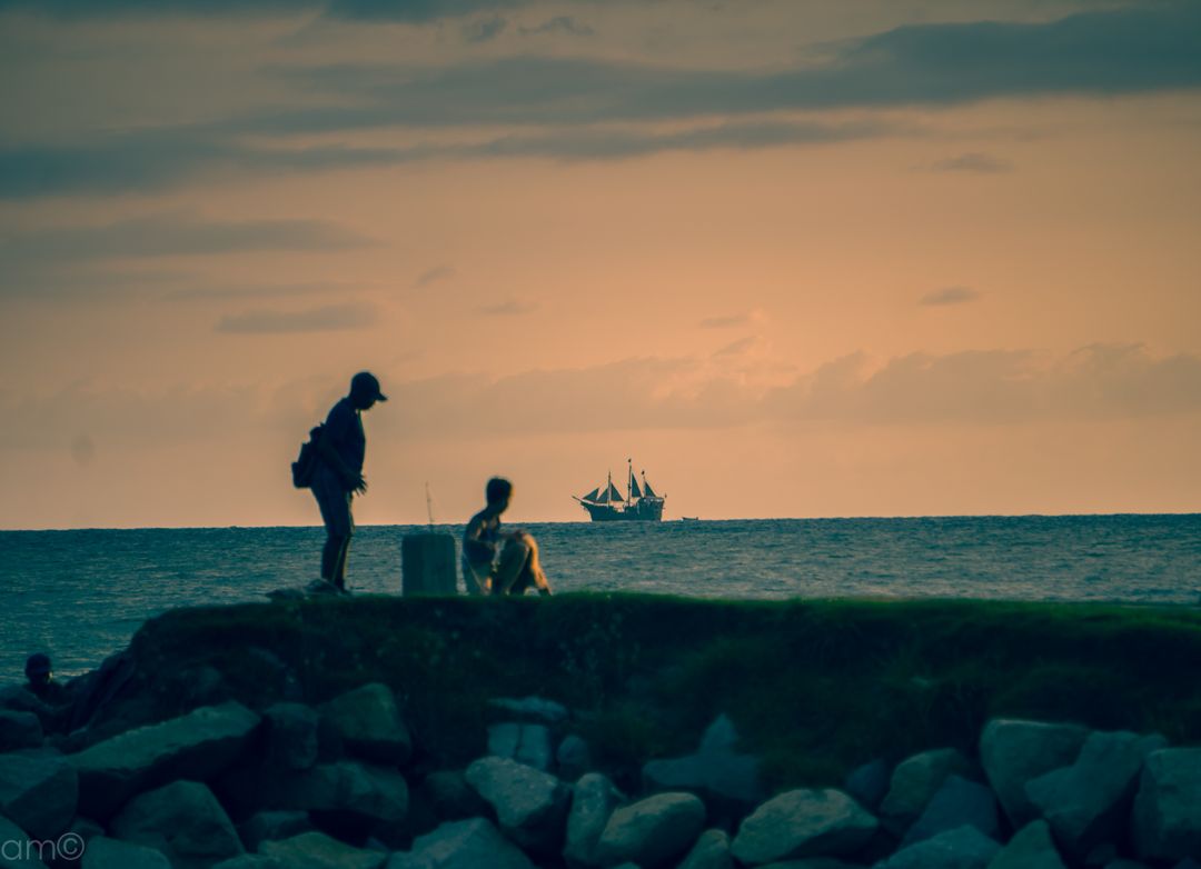 Silhouetted Fishers on Rocky Coast at Sunset with Ship on Horizon - Free Images, Stock Photos and Pictures on Pikwizard.com