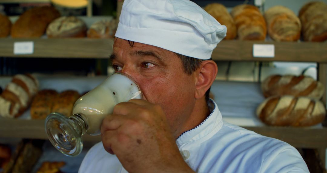 Baker Enjoying Beverage in Bakery with Fresh Bread in Background - Free Images, Stock Photos and Pictures on Pikwizard.com