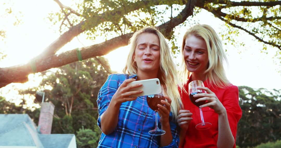 Two Blonde Women Laughing and Taking Selfie While Drinking Wine Outdoors - Free Images, Stock Photos and Pictures on Pikwizard.com