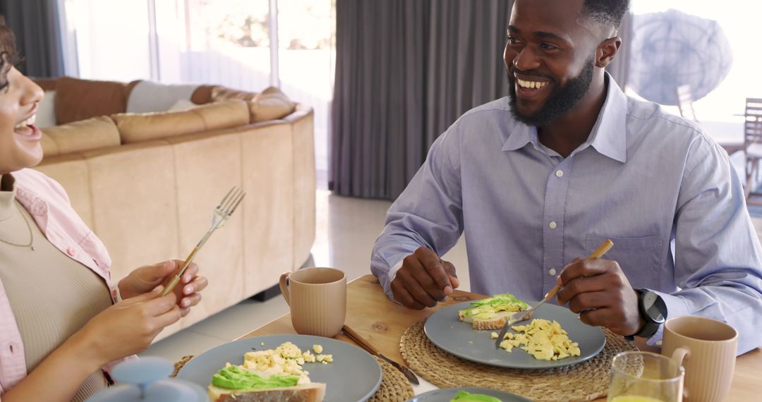 Smiling couple sharing relaxed morning breakfast at home with avocado toast and scrambled eggs