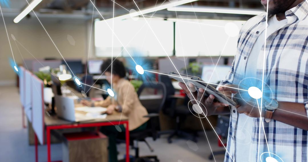 IT professional holding tablet checking network in open-plan office with digital overlay