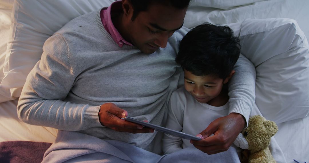 Father and Son Reading Tablet Together in Bed - Free Images, Stock Photos and Pictures on Pikwizard.com