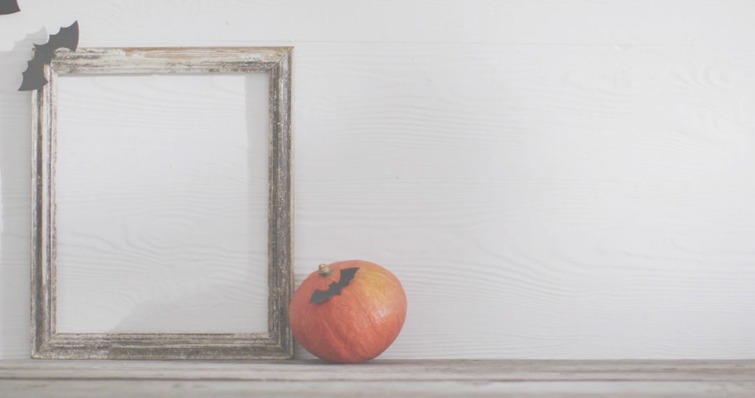 Minimal Halloween Pumpkin Featuring Bat Cutout Beside Rustic Frame on White Wood