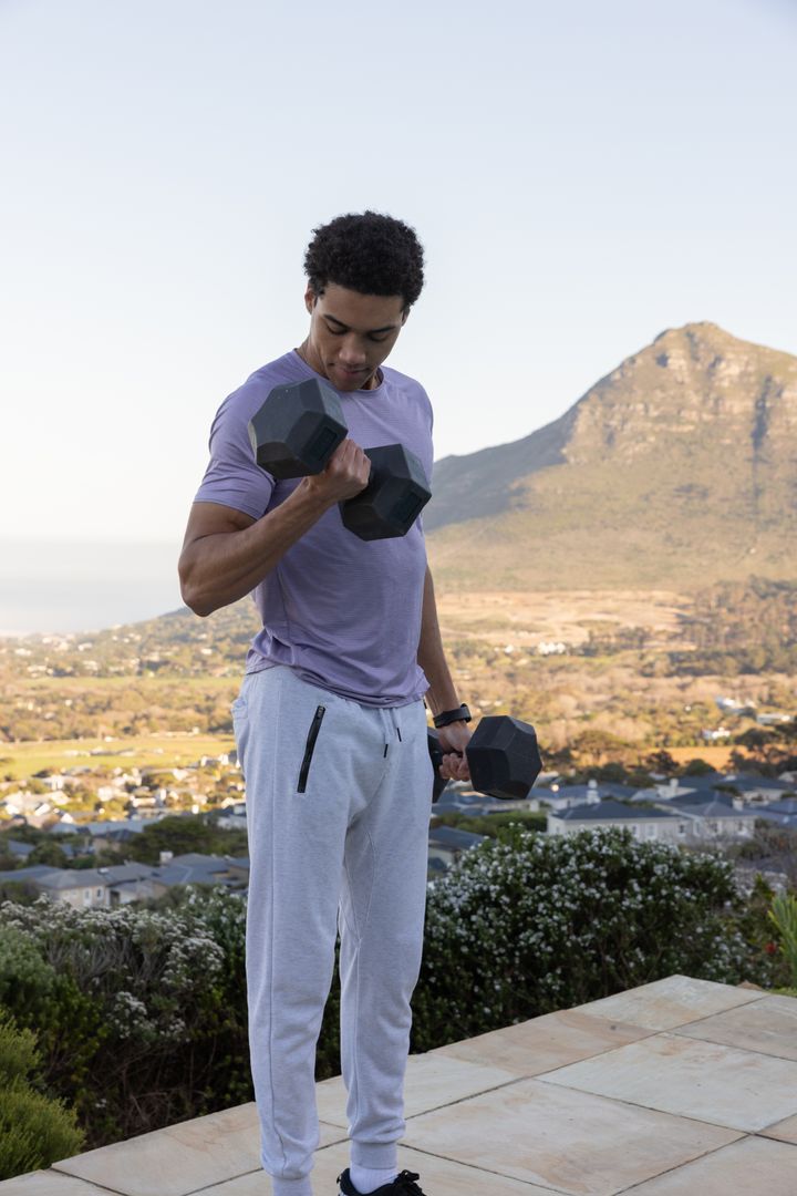 Man Lifting Dumbbells on Terrace with Scenic Mountain View