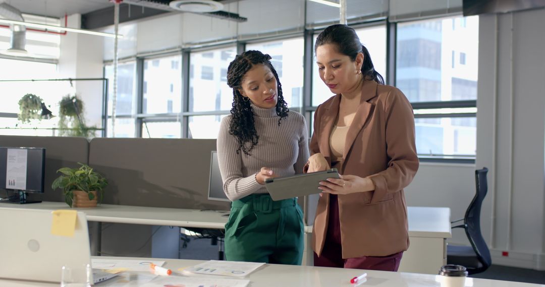 Two Professional Women Collaborating Over Tablet and Documents in Modern Open-Plan Office