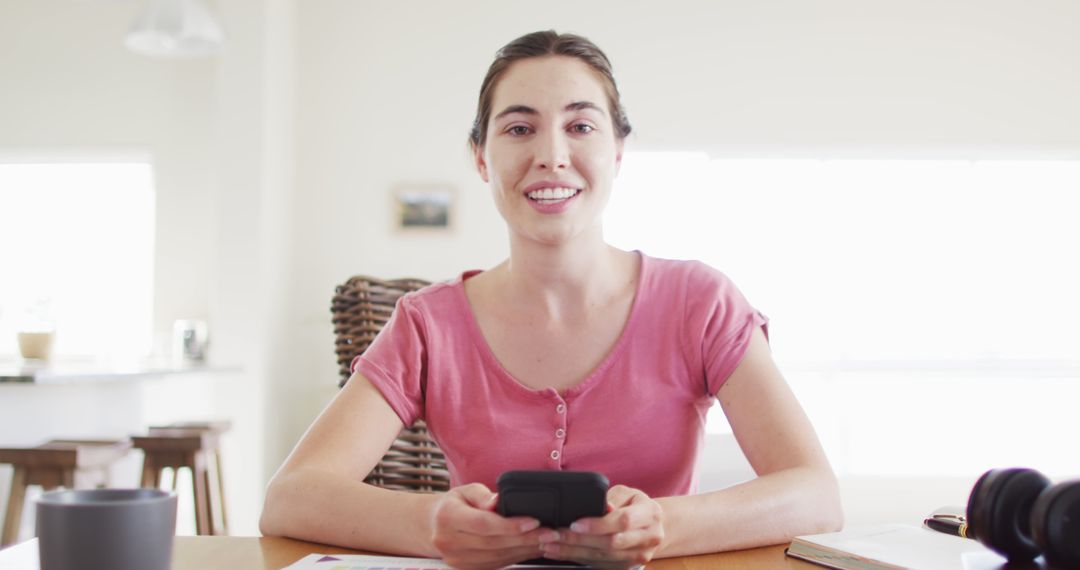 Smiling Woman Holding Smartphone Sitting in Modern Bright Kitchen - Free Images, Stock Photos and Pictures on Pikwizard.com