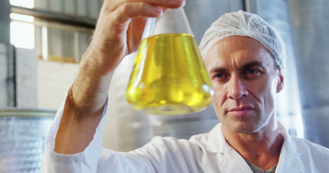 Scientist Wearing Lab Coat and Hairnet Holding Yellow Liquid in Beaker - Free Images, Stock Photos and Pictures on Pikwizard.com