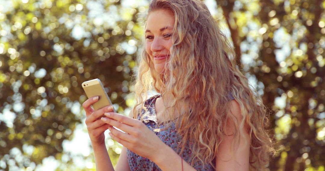 Smiling woman using smartphone in sunlight outdoors - Free Images, Stock Photos and Pictures on Pikwizard.com