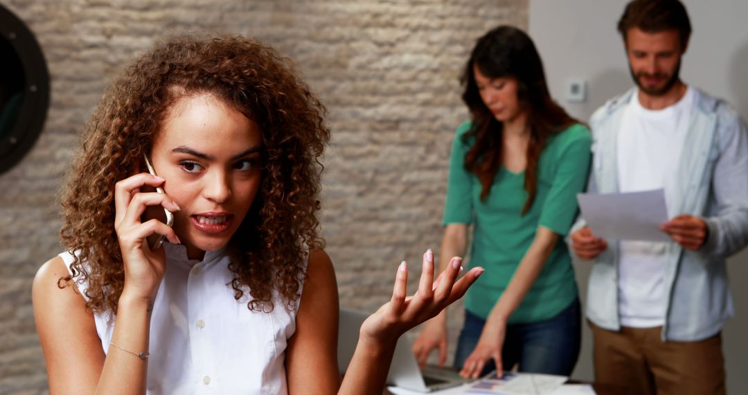 Frustrated Woman on Phone in Office with Colleagues Working in Background - Free Images, Stock Photos and Pictures on Pikwizard.com