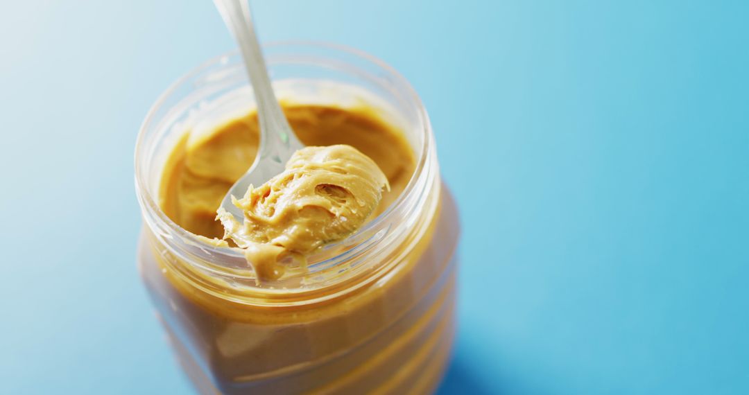 Closeup of Creamy Peanut Butter in Jar with Spoon on Blue Background - Free Images, Stock Photos and Pictures on Pikwizard.com