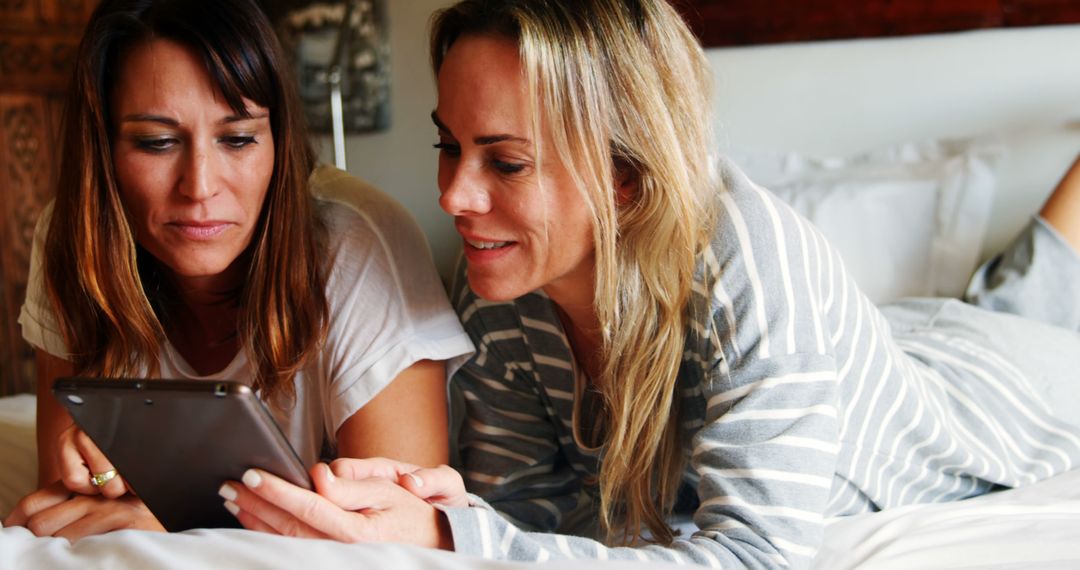 Two Female Friends Relaxing on Bed Using Tablet - Free Images, Stock Photos and Pictures on Pikwizard.com