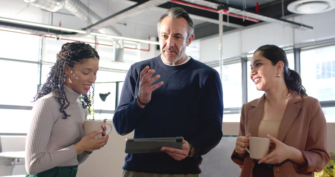 Manager Leading Diverse Team Huddle in Sunlit Open-Plan Office with Tablet and Coffee